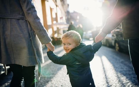 Child Holding Hands With Parents Walking Down Street